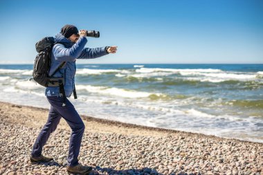 Deniz kıyısındaki bir turist dürbünle bakıp parmağını bir şeye doğrultuyor.