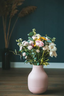 Pembe bir vazoda çeşitli çiçeklerden oluşan güzel bir düzenleme, karanlık bir arkaplan üzerine kurulmuş, bir zarafet ve sükunet hissi uyandırıyor. Konsept: ev dekorasyonu ve çiçek tasarımları