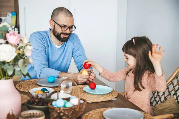 リトルガールと父親は赤いイースターエッグでエッグファイトゲームをして ダイニングテーブルに座った イースターの朝食コンセプトを祝って食べる ストックフォト