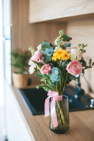 ピンクのリボンで透明なガラスの花瓶に置かれた美しい花束 モダンなキッチンの背景にカウンタートップにセット ストック写真
