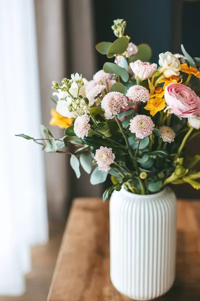 花束一种生机勃勃的花束 摆放在木制桌子上的一个白色有肋的花瓶中 柔和的自然光增强了花的颜色和质地 图库图片