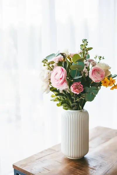 さまざまな色合いとタイプの花の素晴らしい花束は 木製のテーブルの上に立ってリブ付きの白い花瓶を埋めます ストック写真