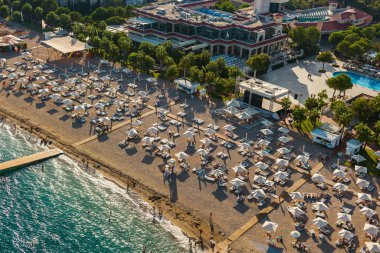 Türkiye 'deki hareketli bir kumsal tatil beldesinin havadan görüntüsü. Beyaz şemsiyelerle dolu bir sahil, ziyaretçilere gölge veriyor.