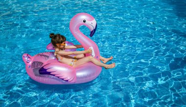 5-6 yaşlarındaki küçük kız pembe flamingo havuzda yüzüyor, yaz aktivitelerini ve çocukların boş zamanlarını vurguluyor.