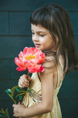 Siyah bir arkaplana karşı büyük pembe bir şakayık çiçeği tutan küçük bir kızın nazik portresi çiçeğin kontrastını ve güzelliğini vurguluyor.