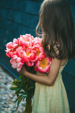 Siyah arka planda büyük bir buket pembe şakayık tutan küçük bir kızın arka planı.