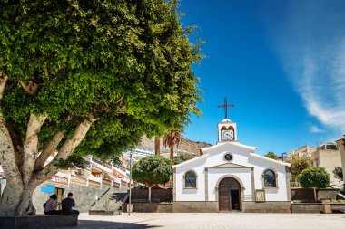 Kutsal Ruh 'un küçük beyaz kilisesi, çapraz çatılı çatısı ve saat süslemeli cephesi, Los Gigantes, Tenerife' de durgun bir dönüm noktası olarak duruyor.