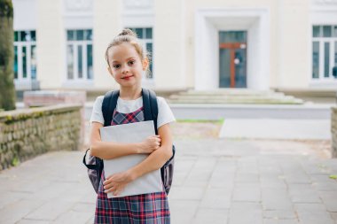 Liseli kız bir kitap tutuyor ve okul binasının önünde dururken sırt çantası takıyor. Okul konseptine dönelim..