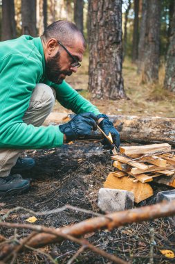 Bir orman bekçisi ormana odun koyarak kamp ateşi yakar.