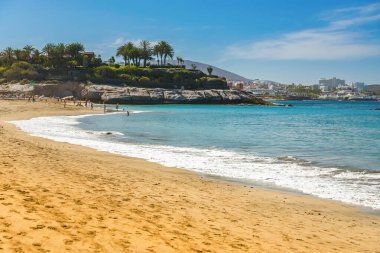 Tenerife 'deki Playa Del Duque' un sakin kıyıları yumuşak kuma vuran berrak dalgaları gözler önüne seriyor. Arka planda canlı yeşillik ile, bu cennet plajı huzurlu bir tatil ya da rahatlama için mükemmel.