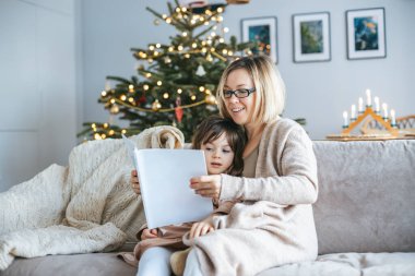 Parlak dekore edilmiş bir Noel ağacının önünde oturan küçük kızına kitap okuyan bir annenin yer aldığı festival sahnesi. Kanepede battaniyenin altına kıvrılıp yatıyorlar. Noel ruhu.
