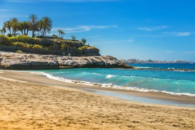 Tenerife 'deki Playa Del Duque' a manzaralı bir manzara, geniş kumlu bir plaj ve sakin turkuaz sularla. Plajın bereketli çevresi ve sakin dalgalar onu rahatlama ve plaj tatili içeriği için mükemmel bir zemin haline getiriyor..