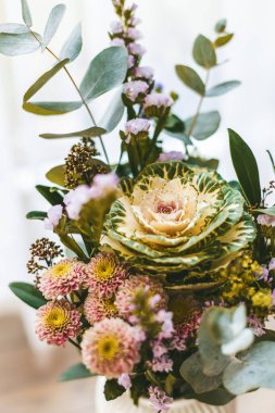 Yakın plan büyüleyici bir çiçek buketi, soluk yeşil lahana çiçekleri sergiliyor, sarı merkezli küçük pembe çiçekler ve yemyeşil