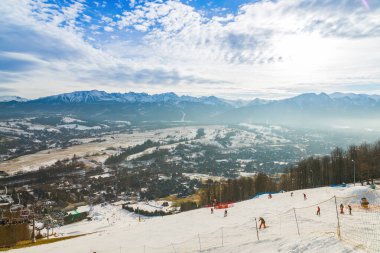 Polonya, Zakopane 'den çarpıcı bir kış sahnesi. Kayakçılar ve snowboardcular karla kaplı yamaçların keyfini çıkarıyorlar. Kış sporları meraklıları ve gezginleri için mükemmel bir görüntü.