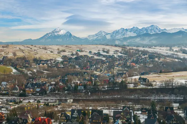 Polonya 'nın Zakopane kentinin büyüleyici panoramik manzarası, bir vadiye yerleştirilmiş alp tarzı binalar. Arka planda Tatra Dağları 'nın karlı zirveleri yükselirken, bariyerli bir yol kasabaya doğru gidiyor.