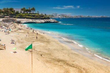 Playa del Duque, Tenerife, insanların güneşlenmekten ve yüzmekten hoşlandığı altın kumlar ve berrak mavi sulara sahiptir. Yeşil bir bayrak güvenli yüzüşü işaret ediyor