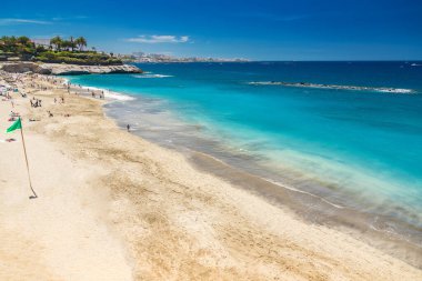 Playa del Duque 'un altın kumları ve kristal berrak sularının keyfini çıkarırken, güvenli yüzme yeşil bir bayrak tarafından belirtildi. Kayalık kayalıklar ve palmiye ağaçları resim sahnesini tamamlıyor.