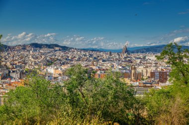 Bu panoramik manzarada, Sagrada Familia Barcelona 'nın siluetine hakim, ağaçlar ve uzak dağlarla çevrili tarihi ve modern mimari bir karışım ile çarpıcı bir zemin oluşturur.