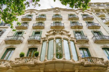 Barcelona 'daki dekoratif yapı cephesinde, karmaşık işlenmiş demir parmaklıklar ve dekoratif taş işçiliğiyle birden fazla balkon yer alıyor. Geniş panelleri ve ayrıntılı oymaları olan bir merkez penceresi. Akan hatları ve doğal motifleriyle Art Nouveau tarzı.