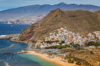 San Andres 'in küçük kasabasının ve Tenerife' deki Las Teresitas plajının güzel hava manzarası. Kasaba renkli binalarla dolu bir yamaçta yuva kurarken, sahil kıyı boyunca altın kum ve berrak mavi sularla uzanıyor.