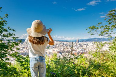Hasır şapkalı genç bir kız, Barcelona 'nın ufuk çizgisine uzaktan görünen ikonik binalar ve simgelerle hayran.