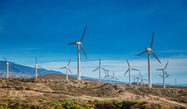 Berrak mavi gökyüzünün altında, İspanya 'nın Tenerife kentindeki uzak dağlarla birlikte, birden fazla rüzgar türbini olan rüzgâr tarlası.