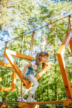 Emniyet kemeri takmış genç bir kız bir orman parkında macera kursuna katılıyor. Meydan okuyan engellerle manevra yaparken ifadesi odaklanma ve heyecandan ibaret.