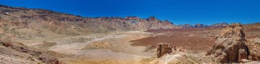 Teide Ulusal Parkı 'nın geniş panoramik manzarası kurak çöl manzarasını ve berrak mavi gökyüzü altında volkanik oluşumlarını gözler önüne seriyor. Engebeli arazi bölgenin doğal güzelliğini vurguluyor