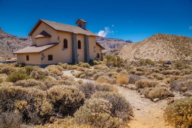 Tenerife 'deki Teide Ulusal Parkı' nda ıssız bir evi olan çöl manzarası. Kuru bitki örtüsüyle çevrili ev, kurak araziye ve dağlık zemin üzerine zıt düşüyor..