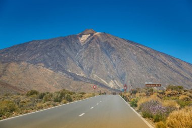 Manzaralı yol Tenerife 'deki ikonik Teide Dağı' na doğru uzanır ve volkanik manzaranın nefes kesici bir görüntüsünü sunar. Açık gökyüzü bu doğal harikanın ihtişamını arttırır..