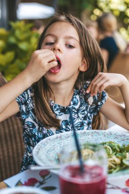 Genç bir kız spagettiyi pesto ile tadıyor, bahçeli bir restoranda dinleniyor.