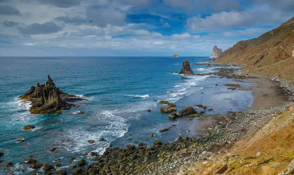 Tenerife 'de kayalık bir Playa Benijo manzarası var. Kuma vuran dalgalar ve kumsalın keyfini çıkaran ziyaretçiler. Dramatik kaya oluşumları berrak mavi gökyüzü ve okyanusun zemininde duruyor.
