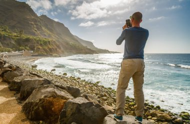 Kayalık sahilde duran kişi, geniş manzaralı okyanus manzarasını akıllı telefon, Playa del Socorro, Tenerife ile yakalıyor. Engebeli uçurumlar ve çarpan dalgalar, seyahat fotoğrafçılığı için ideal, resim gibi ve ilham verici bir atmosfer yaratıyor.