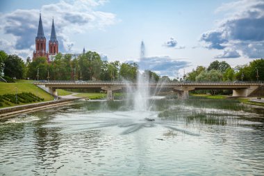 Bereketli yeşilliklerin arasından bakan kırmızı tuğlalı bir kilisenin çift kuleleri, sakin suların üzerindeki pitoresk bir çeşme ve köprünün yanında herhangi bir Litvanya 'nın büyüleyici manzarası.