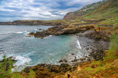 Tenerife 'deki El Sauzal' ın dramatik kayalık kıyıları yemyeşil ve sakin sularla çevrili. Dalgalar yavaşça kayalara çarpar, sakin ve huzurlu bir manzara yaratır.