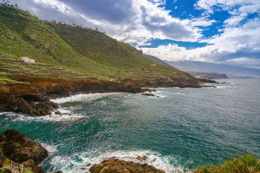 Tenerife 'deki Costa de El Sauzal' da çarpıcı bir kıyı manzarası; yemyeşil yamaçlar, teraslı yamaçlar, engebeli uçurumlar ve parçalı bulutlu bir gökyüzü altında geniş Atlantik Okyanusu 'na sahiptir.