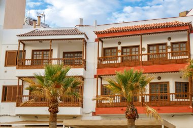 Candelaria, Tenerife 'de ahşap balkonları ve terracotta çatı kiremitleri olan geleneksel renkli evler, mavi gökyüzünün altında beyaz ve turuncu cepheler ve palmiye ağaçları yer alıyor.