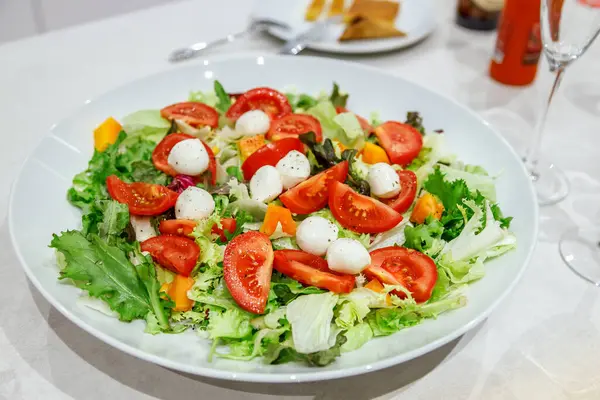 Sağlıklı vejetaryen salatası, karışık yeşillikler, kiraz domatesleri ve mozarella topları, beyaz bir kasede sunuluyor, tazelik ve sağlıklı yaşam tarzı seçenekleri gösteriliyor.