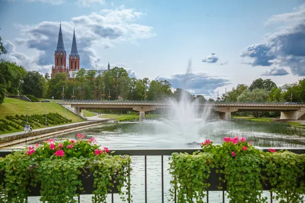 Litvanya, Anyksciai 'de yüksek kuleleri olan güzel bir kilisenin manzarası. Çağdaş bir köprünün altından bir nehir akıyor, yeşil ve çiçeklerle çevrili canlı bir çeşme.