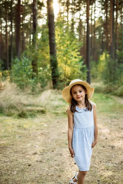 Hasır şapkalı ve mavi elbiseli genç bir kız ağaçlar ve yeşilliklerle çevrili güneşli bir ormanda yürüyor. Macera ve masumiyet ruhunu somutlaştırıyor.