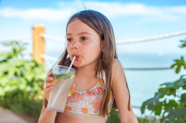 Etrafı yaz atmosferiyle çevrili, plaj şemsiyeleri altında alkolsüz mojito içen genç bir kızın portresi.