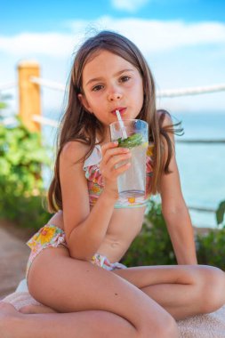 Plaj kenarı sükuneti. Bir kız alkolsüz naneli mojito yudumlarken, geniş güneş şemsiyelerinin gölgesinde bir havluya rahatça otururken.