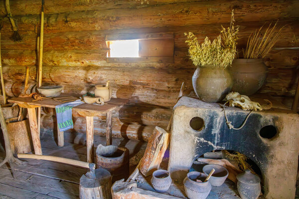 Rustic wooden cabin interior with clay pots, dried plants, axe in stump and natural light through shuttered window