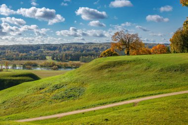 Litvanya 'daki dramatik bulutlu sonbahar gökyüzü altında Kernave arkeolojik alanı saran toprak yolu ile yeşil çimenler gömülü.