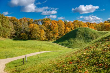 Kernave 'in yeşil tepeciklerinin manzarası. Sonbahar yapraklı ve beyaz bulutlu parlak mavi gökyüzü olan bir ormana karşı tarihi rezerv.