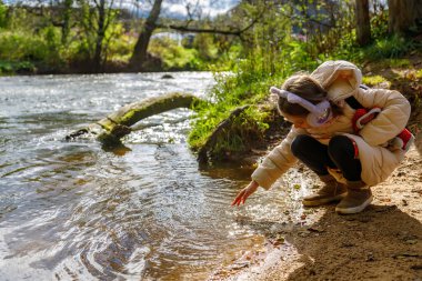 Sıcak paltolu genç bir kız güneşli bir sonbahar gününde ışıl ışıl bir nehrin kenarında çömeliyor, eli nazikçe suyun yüzeyine dokunuyor, masumiyeti, oyunculuğu ve doğayla olan bağlantısını aktarıyor.