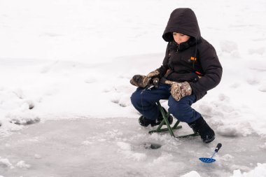 Fotoğraflar Rost 'un buzdaki bir deliğin yanındaki katlanır sandalyede oturduğunu gösteriyor. Kışlık kalın kıyafetler giyiyor: kapüşonlu siyah bir ceket, koyu mavi pantolon, kamuflaj desenli eldivenler ve siyah botlar. Ön planda kış için bir delik var. 