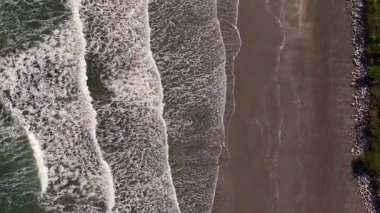 Okyanus dalgalarının tepeden tırnağa sahile çarpan 4K hava aracı görüntüleri. Video kumun dokusunu, köpüklü dalgaları vurguluyor.
