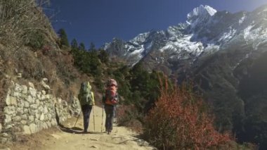 İki kadın sırt çantalı Himalaya dağ yolunda yürüyor. Sagarmatha Ulusal Parkı, EBC, Nepal. Karlı dağlara bak. 4K, UHD
