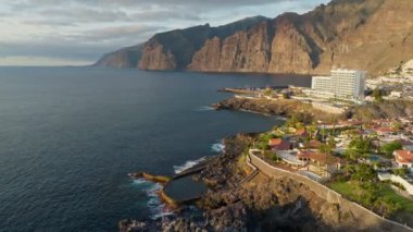 Aerial view of Los Gigantes restort on Tenerife Canary island. Flying over magnificent hotels, villas and natural pool on the ocean - rocks in sunset light in the background. Canary islands, Spain